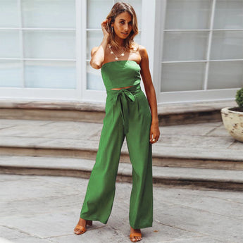 Beige tie-waist sleeveless jumpsuit displayed on a person, showcasing its elegant and casual summer style, with a focus on the waist and thigh areas. The background includes a flowerpot with a houseplant, enhancing the casual and stylish atmosphere.