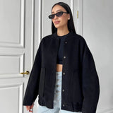 A woman wearing a black oversized fleece bomber jacket with a trendy winter design, featuring a prominent collar and long sleeves. The jacket is styled in a casual outdoor setting with matching sunglasses, showcasing the fashionable aspect of the winter wear.