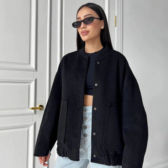 A woman wearing a black oversized fleece bomber jacket with a trendy winter design, featuring a prominent collar and long sleeves. The jacket is styled in a casual outdoor setting with matching sunglasses, showcasing the fashionable aspect of the winter wear.