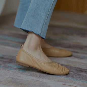 
Beige women's soft leather ballet flats, flexible slip-on shoes, displayed on a wooden floor.
