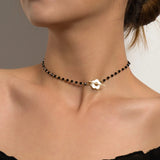 A woman wearing a black bead choker necklace with a gold bird pendant against her skin.