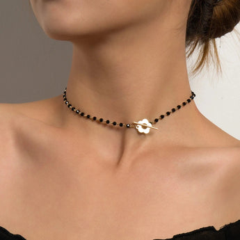 A woman wearing a black bead choker necklace with a gold bird pendant against her skin.
