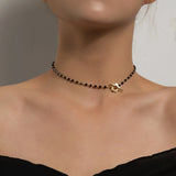 Minimalist black bead choker necklace with gold bird pendant displayed on a model's neck and shoulder area.