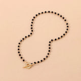 Black bead choker necklace with a gold bird pendant, featuring minimalist nature-inspired jewelry design.