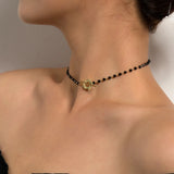 Black bead choker necklace with gold bird pendant worn around a woman's neck, highlighting minimalist nature jewelry style.