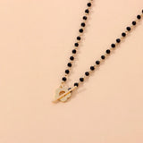Black bead choker necklace with a gold bird pendant, minimalist nature jewelry displayed on a wooden surface.