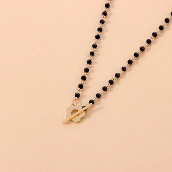 Black bead choker necklace with a gold bird pendant, minimalist nature jewelry displayed on a wooden surface.
