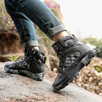 Black camo tactical waterproof hiking boots being worn outdoors on grass, showcasing rugged design and high-traction soles, with a cool grey color scheme.