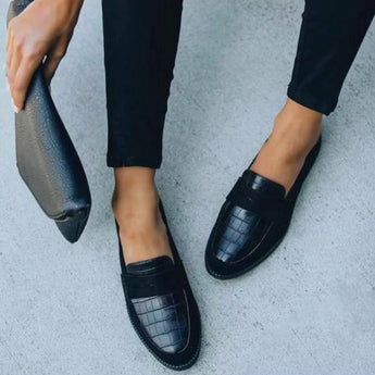 Black crocodile loafers for women, luxury designer slip-on shoes, black color, size 43, modeled with grey denim jeans, standing position.