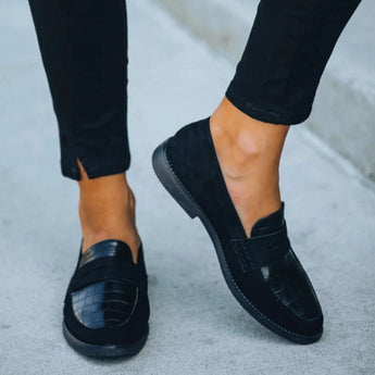 Black crocodile loafers for women, luxury designer slip-on shoes, paired with grey denim pants.