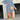 A model wearing a black denim dress paired with a fringe purse and western ankle boots, styled with blue accents, showcasing the XXL size variant. The model is accessorized with sunglasses, adding a chic touch to the western-inspired outfit.