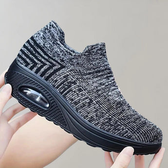 Black knit slip-on sneakers designed for breathability and lightweight comfort, showcased against a sportswear-themed background.