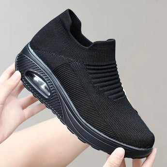 Black knit slip-on sneakers worn on a human leg, showcasing their breathable and lightweight design, with a focus on the athletic shoe's features.