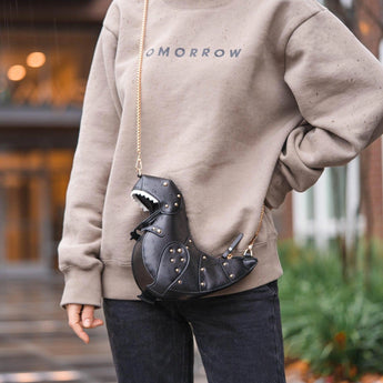 Black leather horse-shaped crossbody bag with a gold chain strap displayed against a backdrop of fashionable clothing items and accessories.