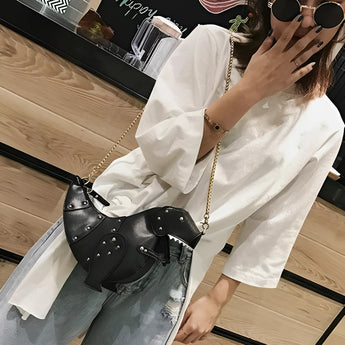 Black leather horse-shaped crossbody bag with a gold chain strap worn over a shoulder, paired with a dress shirt and sunglasses.