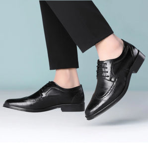 Men's black leather Oxford shoes displayed from a side angle, showcasing their formal brogue design with lace-up closure, paired with blue denim jeans.