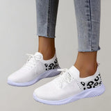 Black leopard print women's stylish comfortable sneakers shown on a white and grey textile background with a plant in the vicinity.