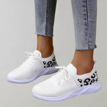Black leopard print women's stylish comfortable sneakers shown on a white and grey textile background with a plant in the vicinity.