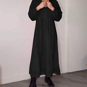 
A woman wearing a black maxi dress with long sleeves and a crew neck, featuring a loose fit perfect for fall fashion. The dress reaches down to her knees and is styled in a sophisticated, elegant manner ideal for formal wear.