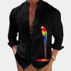 A black men's casual shirt with a colorful exotic parrot graphic, featuring long sleeves, a collar, and worn by a person with a visible hand and arm.