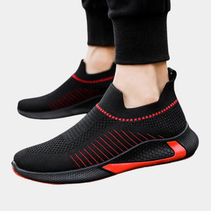 Black men's slip-on sneakers featuring breathable mesh material and red accents, designed with a flexible sole suitable for outdoor and walking activities.