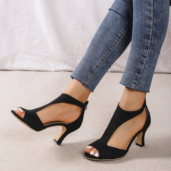 Black peep-toe heels with a comfortable low heel, worn by a person with exposed legs, featuring a sleek and elegant design suitable for summer wear.