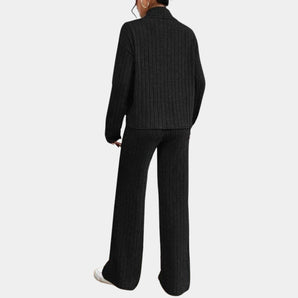 Black ribbed knit jumpsuit, featuring long sleeves and a full-length design, ideal for elegant winter wear. The outfit has a sophisticated look with a structured collar and a form-fitting silhouette.
