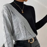 Black ribbed knit turtleneck sweater featuring chunky contrast sleeves, with a blend of black, white, and grey colors.