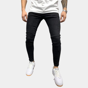 Black stretch skinny jeans for men in a trendy urban style, size 3XL, showcasing a slim fit design on a male model. The focus is on the jeans, highlighting their fit and style, along with some visible parts of the human body such as the legs and knees.