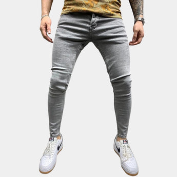 Gray stretch skinny jeans for men in a slim fit, showcasing a trendy urban style, with focus on the leg area and waist, worn with white shoes.