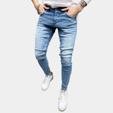 Light blue stretch skinny jeans for men in a slim fit, highlighting a trendy urban style. The jeans are made of denim and are displayed on a model who is wearing a white top and grey outerwear.