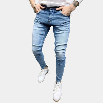Light blue stretch skinny jeans for men in a slim fit, highlighting a trendy urban style. The jeans are made of denim and are displayed on a model who is wearing a white top and grey outerwear.