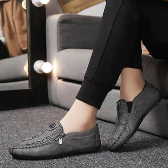 Black textured leather slip-on loafers with a zipper for men, displayed on a gray background, highlighting the sleek design and comfortable fit suitable for dress occasions.