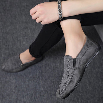 Black textured leather slip-on loafers for men featuring a zipper, shown on a model wearing grey dress pants.