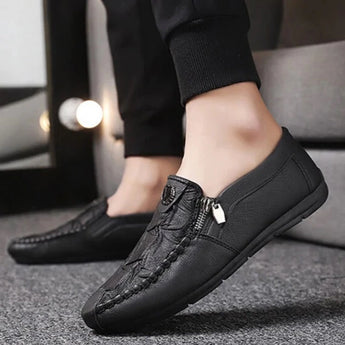 Black textured leather slip-on loafers with zipper for men, featuring a sleek design, shown worn on a human leg with a formal dress style suitable for fashion-forward occasions.
