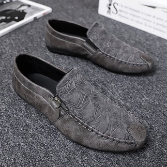 Black textured leather slip-on loafers with zipper for men displayed against a neutral background, showcasing the leather's natural pattern and fashion-forward design.