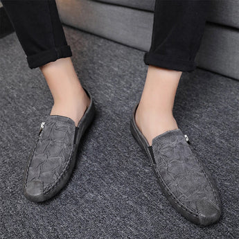 Men's black textured leather slip-on loafers with zipper, shown on a person wearing blue denim jeans, standing on a grey floor surface.