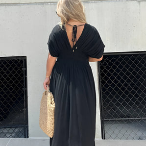 Black V-Neck Open Back Maxi Dress on woman with short sleeves, showcasing shoulder and waist details, accessorized with a bag and eyewear.