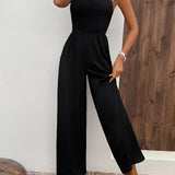 Black velvet sleeveless wide-leg jumpsuit with a smocked bodice, featuring a scooped neck and fitted waist, displayed on a mannequin against a neutral background.