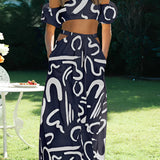 Off-shoulder black and white abstract patterned two-piece dress with a palazzo pants set, shown in Blu Navy color and XL size, styled with high heels, displayed in an indoor setting with a window and greenery in the background.
