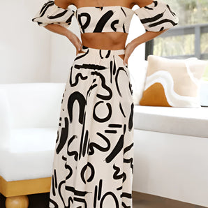 Black and white abstract two-piece dress featuring an off-shoulder top and palazzo pants, worn by a smiling model with visible arms and shoulders.