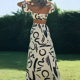 Black and white abstract two-piece dress featuring an off-shoulder top and palazzo pants, modeled outdoors with a natural background.
