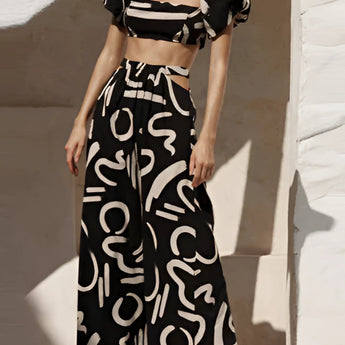 
A black and white abstract two-piece dress featuring an off-shoulder top and palazzo pants, displayed on a fashion model.