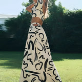 Black and white abstract two-piece dress featuring an off-shoulder top and palazzo pants, modeled outdoors against a backdrop of trees and grass, showcasing a blend of fashion design and leisure.