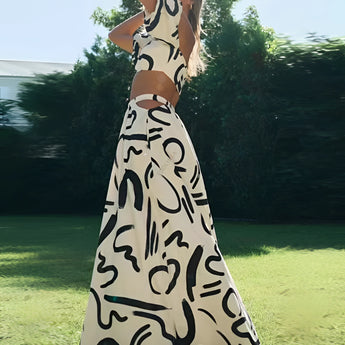 Black and white abstract two-piece dress featuring an off-shoulder top and palazzo pants, modeled outdoors against a backdrop of trees and grass, showcasing a blend of fashion design and leisure.