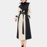 Black and white belted trench coat in a monochrome chic style, featuring a collar and long sleeves, worn by a standing model.