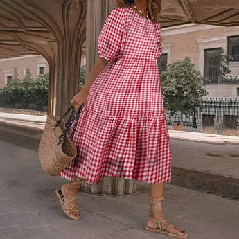 Red and black midi dress in a classic black & white gingham pattern with puff sleeves, displayed over a wooden trunk on a sidewalk.