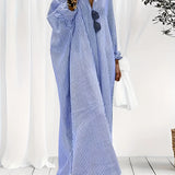 A woman wearing a black and white striped maxi dress with long sleeves, suitable for breezy beachwear. The dress is styled in a blue color variant, size 3XL. She accessorizes with sunglasses. The dress features a defined waist and covers the shoulders and arms.