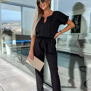 Black women's summer jumpsuit, chic and lightweight, worn by a smiling woman with sunglasses, showcasing an elegant fashion look with short sleeves and an exposed neckline.