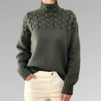 
A gray wool cable knit turtleneck sweater modeled by a woman, showcasing its long sleeves and intricate knit pattern. The sweater is styled for fall fashion and is available in size 2XL.